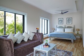 A bedroom with a bed, a sofa, a coffee table, and a window with a view of palm trees. - Oxel town house (Oxel)