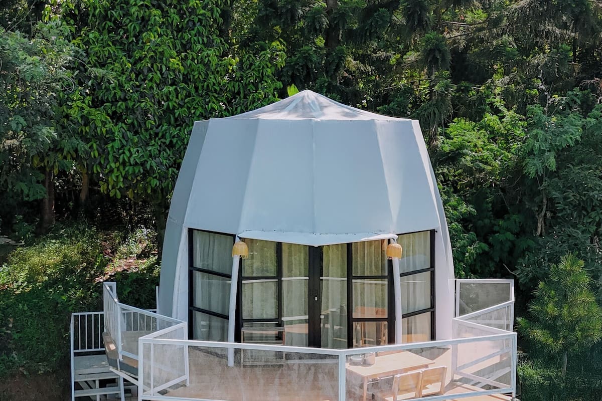 Une structure en forme de dôme géodésique dotée d’un balcon, entourée de verdure.