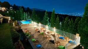 A rooftop pool area with outdoor seating and a view of the city lights. - Luxcamp Bukit Damar - Puncak By Horison (Megamendung)