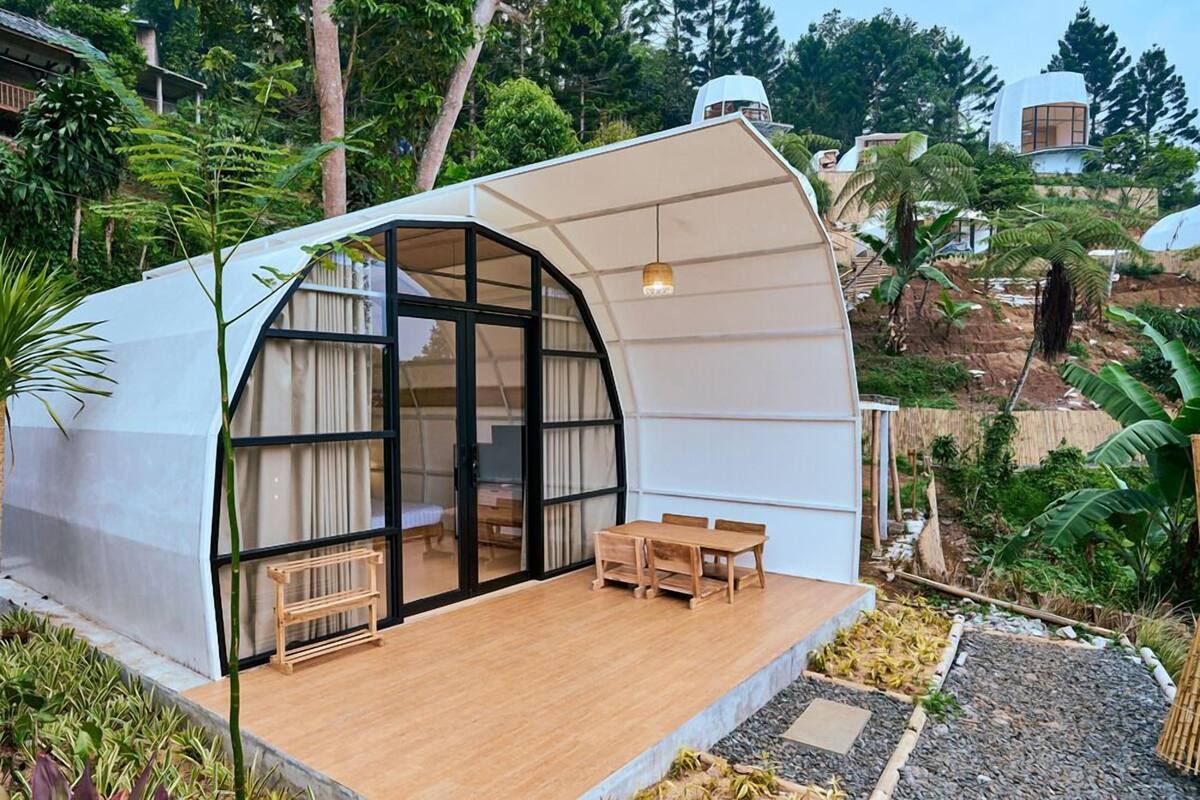 Une structure moderne, partiellement ouverte, dotée d’une terrasse en bois, de portes vitrées, ainsi que d’une petite table et d’un banc.