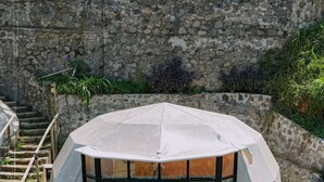 A hexagonal structure with a glass facade, a wooden deck, and a stone wall in the background. - Luxcamp Bukit Damar - Puncak By Horison (Megamendung)