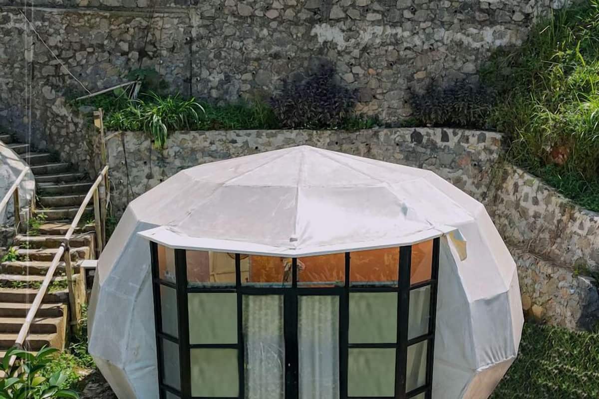 Une structure hexagonale dotée d’une façade en verre, d’une terrasse en bois et d’un mur de pierre en arrière-plan.