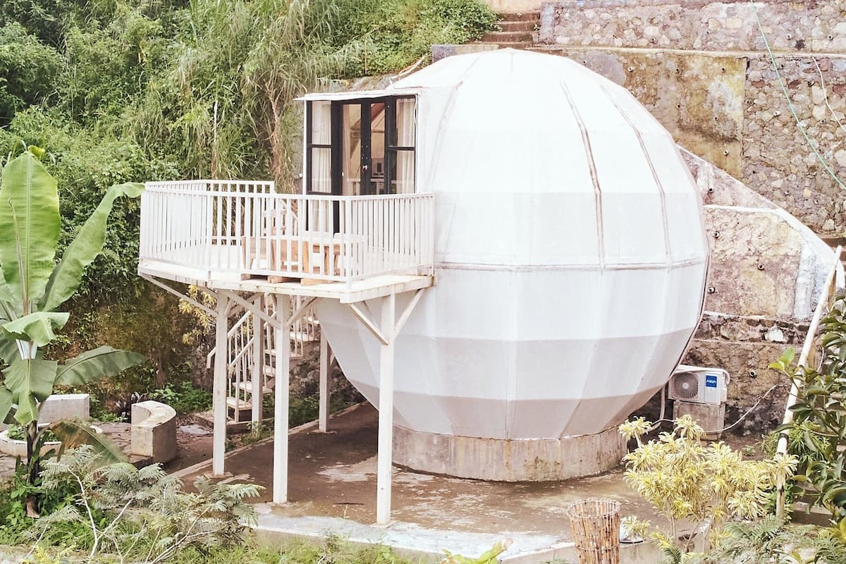 Une structure sphérique dotée d’un balcon, entourée de verdure.