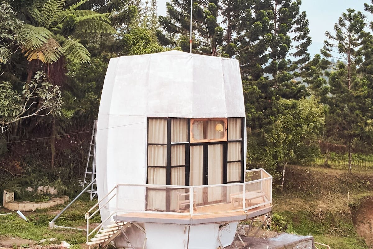 Un petit bâtiment blanc, de plain-pied, doté d’un balcon et d’une fenêtre avec des rideaux.