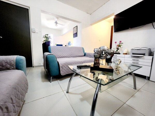 A modern living room with a glass coffee table, a sofa, a TV, and a printer.