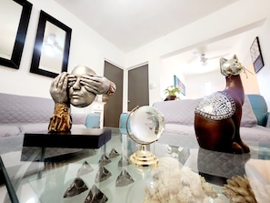 A living room with a glass coffee table, a sofa, and a decorative sculpture.