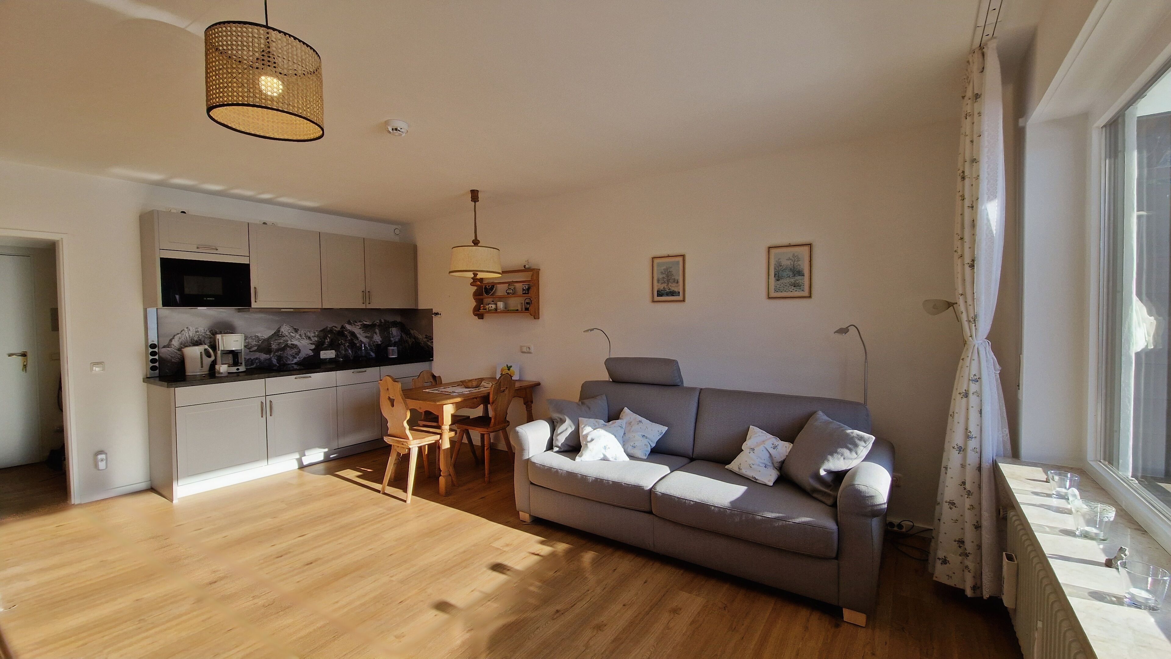 Ein modernes Wohnzimmer mit grauem Sofa, Holzes Esstisch und einer Küche im Hintergrund.