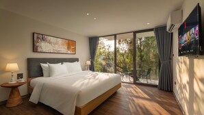 Ein Hotelzimmer mit einem Bett, einem Fernseher, einem Gemälde und einem Balkon mit Stühlen.