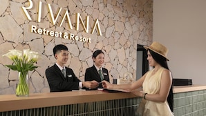 Ein Empfangstresen im Rivana Retreat & Resort, mit einer Wand aus Stein im Hintergrund und einer Vase mit weißen Blumen.
