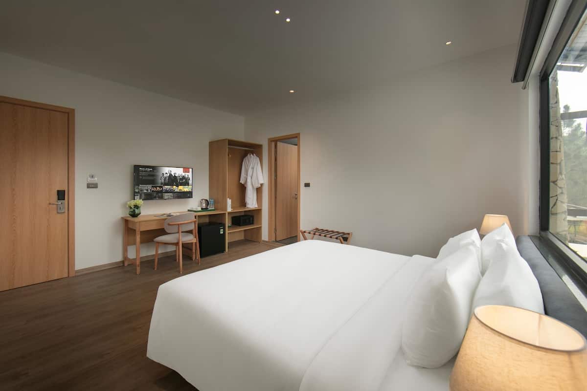 A modern hotel room with a large bed, a desk with a chair, a wardrobe, and a television.