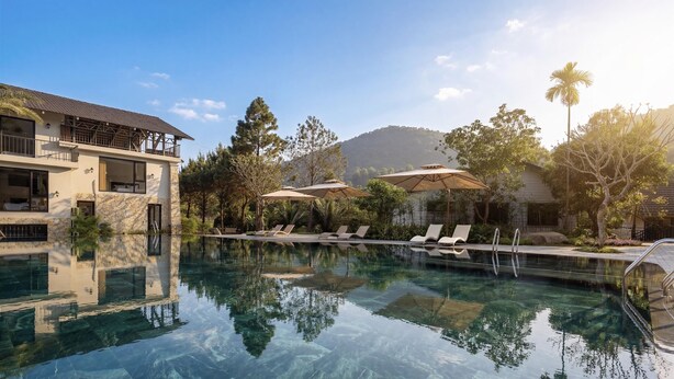 Ein klares Schwimmbecken mit Liegestühlen, ein Gebäude mit Balkon und umliegende Bäume.