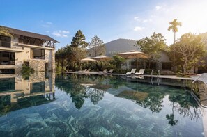 A clear swimming pool with lounge chairs, a building with a balcony, and surrounding trees. - Rivana Retreat (Hanoi)