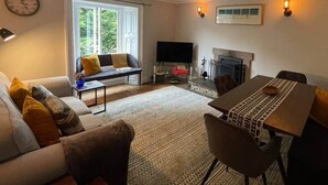 A living room with a sofa, a dining table, a fireplace, and a television. - Peak District Retreat · Hope Valley · Dogs Welcome (Stoney Middleton)