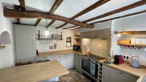 A compact kitchen with a central island, built-in appliances, and exposed wooden beams. - Peak District Retreat · Hope Valley · Dogs Welcome (Stoney Middleton)