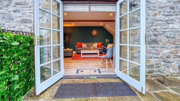 An open doorway to a living room with a sofa, coffee table, and a clock on the wall. - Stylish Bakewell Cottage with Free Parking (Bakewell)
