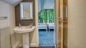 A bathroom with a sink, mirror, and a view into a bedroom with two beds and a forest-themed wall. - Stylish Bakewell Cottage with Free Parking (Bakewell)