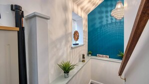 A hallway with a white wall, a blue accent wall, a hanging chandelier, a potted plant, and a small decorative item on a shelf. - Stylish Bakewell Cottage with Free Parking (Bakewell)