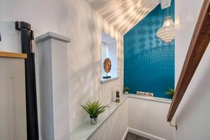 A hallway with a white wall, a blue accent wall, a hanging chandelier, a potted plant, and a small decorative item on a shelf. - Stylish Bakewell Cottage with Free Parking (Bakewell)