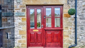 A red double door with glass panels, a stone wall, and a small green plant on the right. - Stylish Bakewell Cottage with Free Parking (Bakewell)
