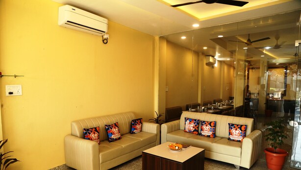 A living room with a beige sofa set, a coffee table, and a potted plant. - JMC HOTEL KIA INN (Pithampur)