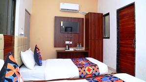 A hotel room with a bed, a television, a desk with a kettle, and a wardrobe. - JMC HOTEL KIA INN (Pithampur)