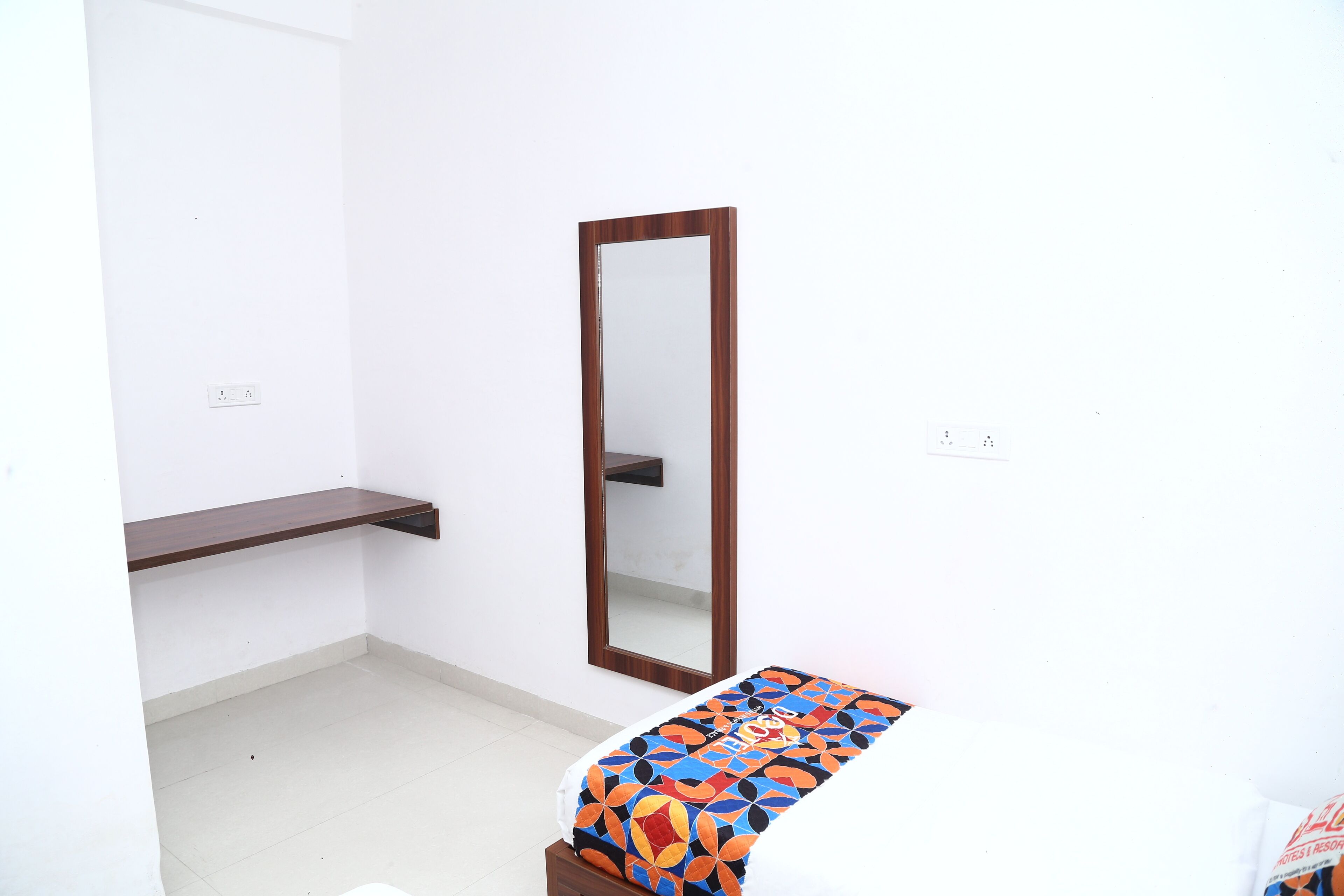 A room with a bed, a bedside table, a mirror, and a shelf.