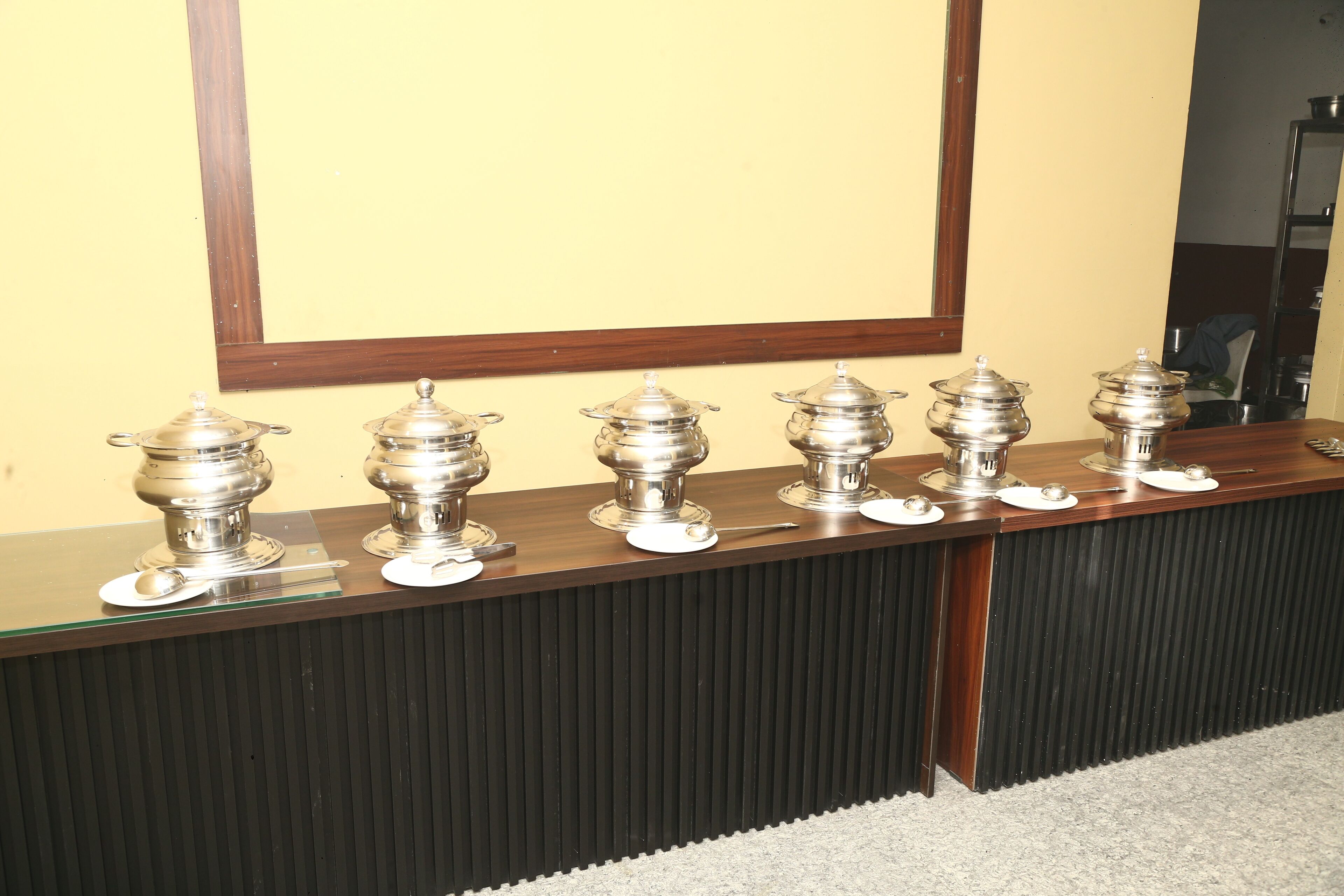 A long wooden reception desk with multiple silver serving dishes and spoons.
