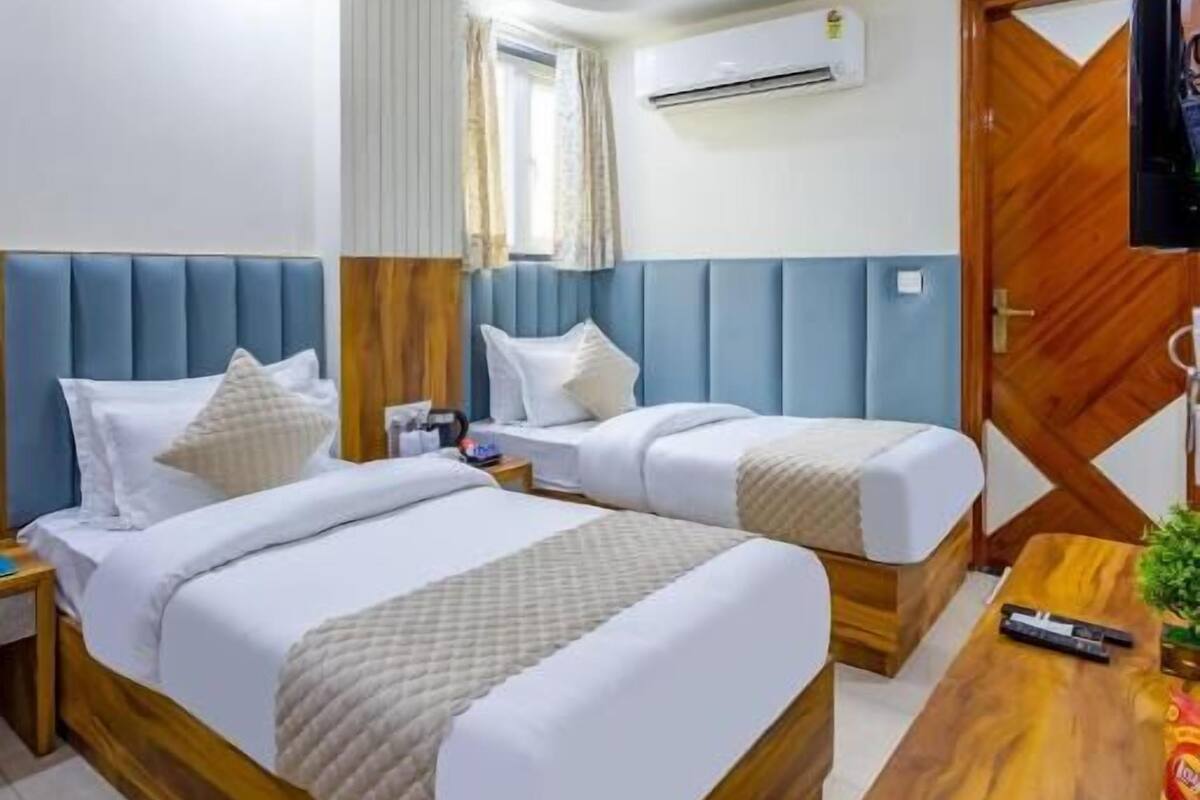 Une chambre d’hôtel avec deux lits, un ventilateur de plafond, un appareil de climatisation, un bureau en bois et un téléviseur.