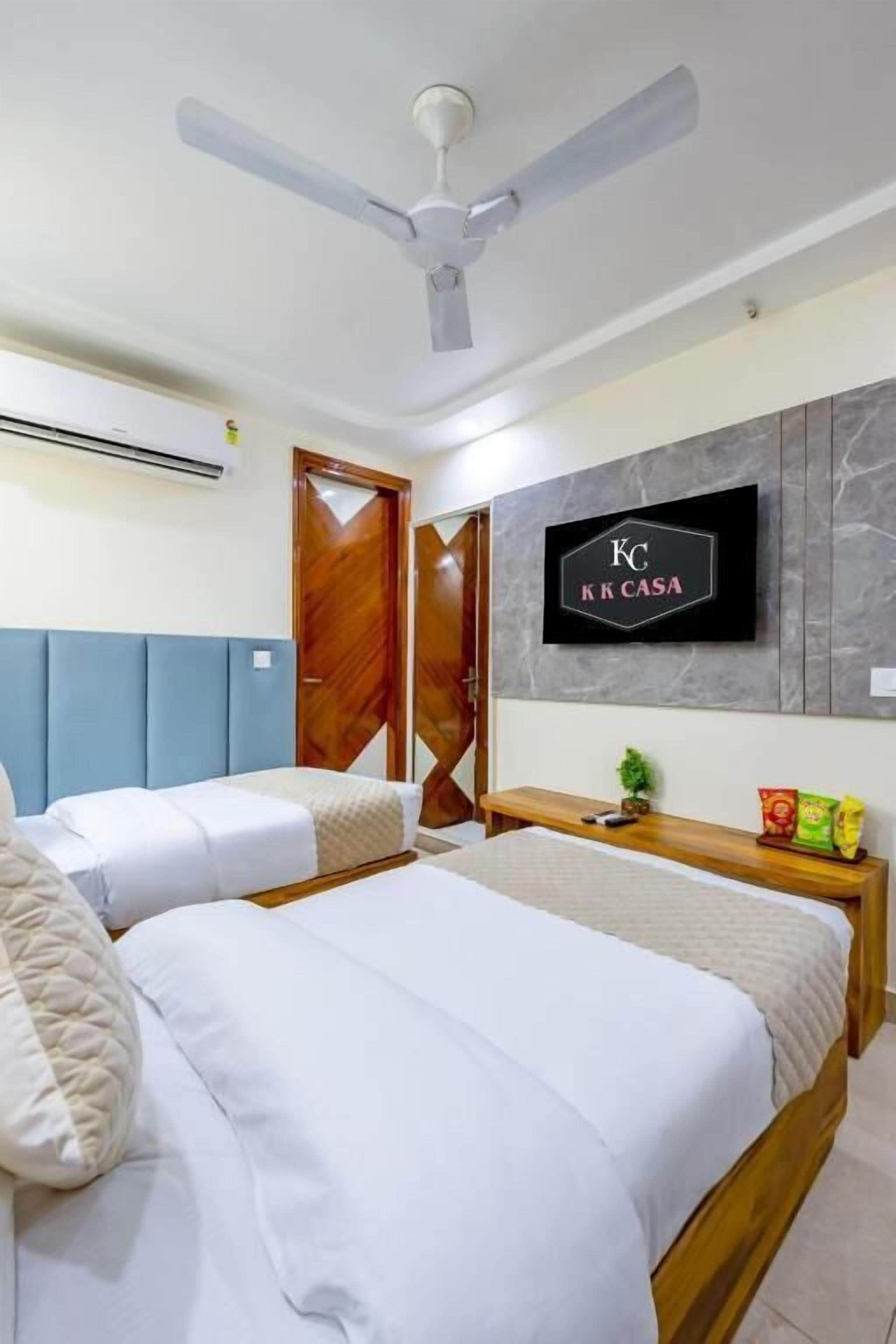 Habitación de hotel con dos camas, ventilador de techo, televisor montado en la pared y cabecero de madera.