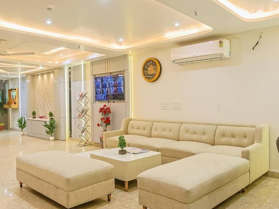 A modern living room with a sofa, ottomans, a flat-screen TV, decorative items, and an air conditioning unit.