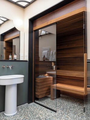 Un baño moderno con un lavamanos blanco, tocador de madera y mampara de ducha de vidrio.
