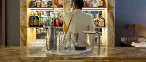 A bar area with a bartender preparing a drink, a variety of liquor bottles on shelves, and a marble countertop.