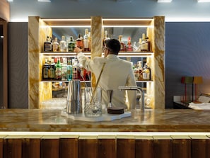 A bar area with a bartender preparing a drink, a variety of liquor bottles on shelves, and a marble countertop. -  Elizabeth Unique Venice a Member of Design Hotels (Venice)