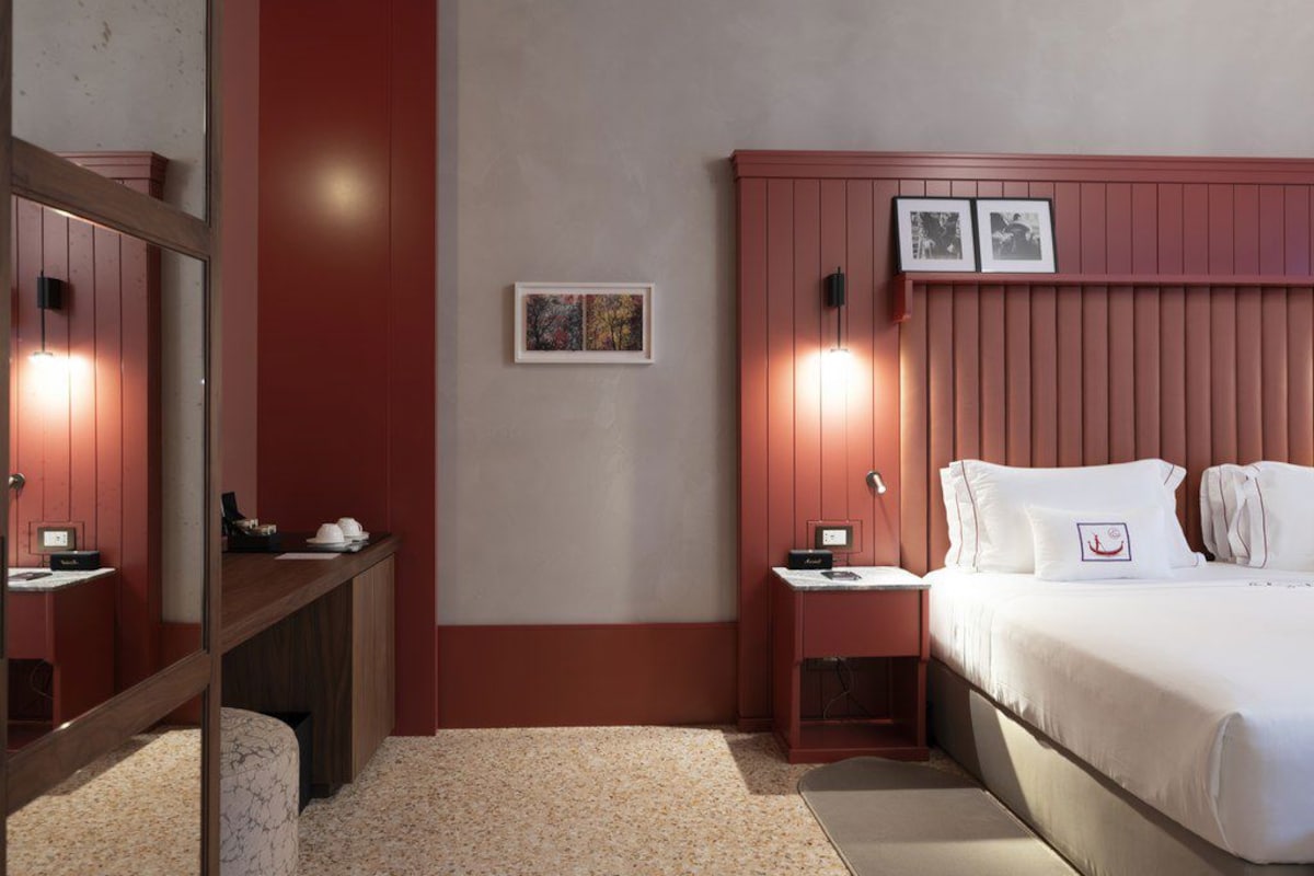 Une chambre d’hôtel avec un lit, des tables de chevet, un miroir et des œuvres d’art accrochées au mur.