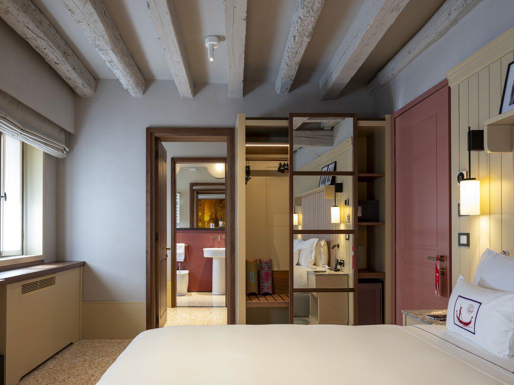 A hotel room with a large bed, a wardrobe, a bathroom with a sink, and a view of the hallway.