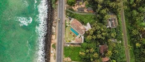 Vista aérea de una propiedad costera con piscina, camino y vegetación densa.