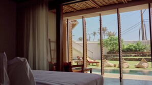 A hotel room with a bed, a view of a pool, and a balcony with seating. - UNU Boutique Hotel (Ahangama)
