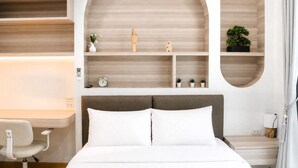 A hotel room with a bed, a desk, and shelves with plants and a clock. - Dinnano (Khlong Thom)