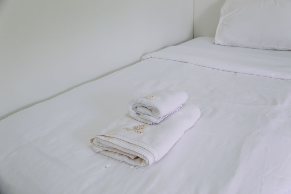 A neatly made bed with white linens and a rolled towel.