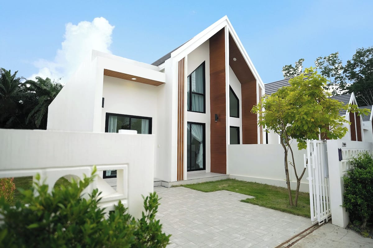 A modern two-story house with a white exterior, large windows, and a small front yard.