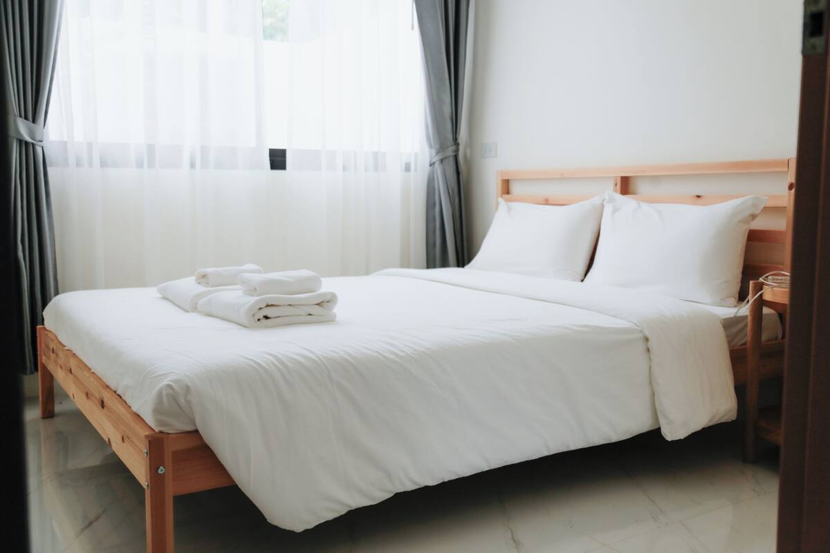 A neatly made bed with white linens and towels, a wooden headboard, and a bedside table with a lamp.