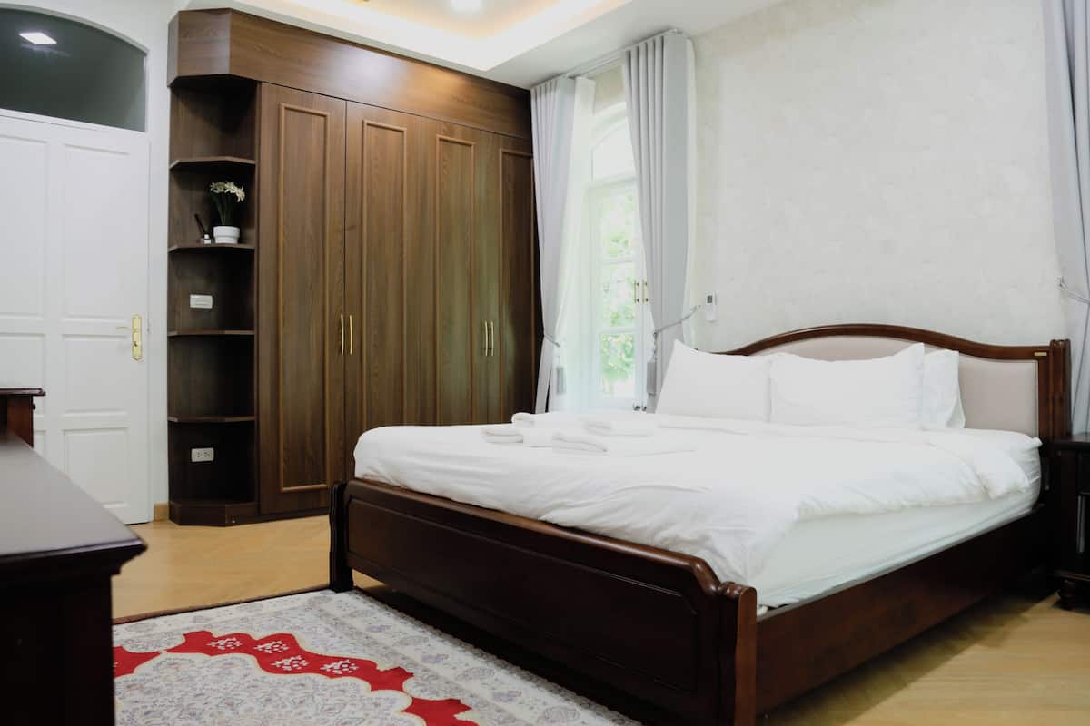 A bedroom with a wooden bed, a wardrobe, and a small shelf with a plant.