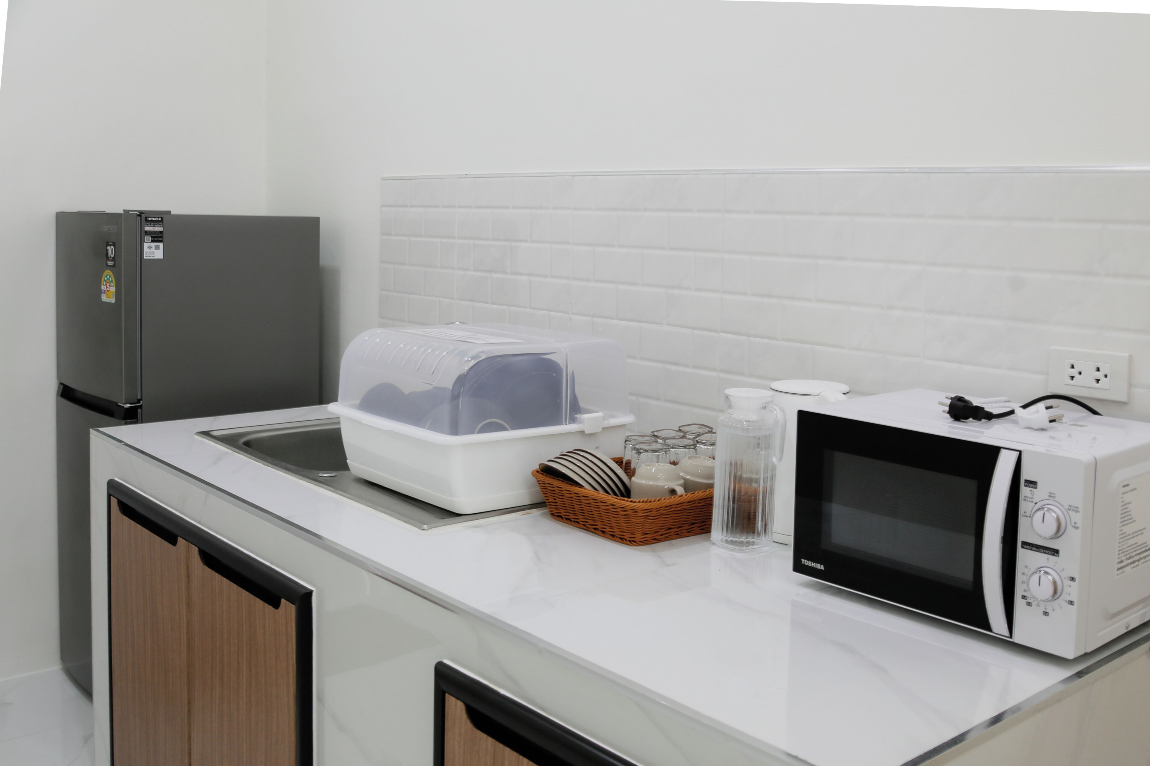 A kitchen with a refrigerator, microwave, sink, and a dish drying rack.