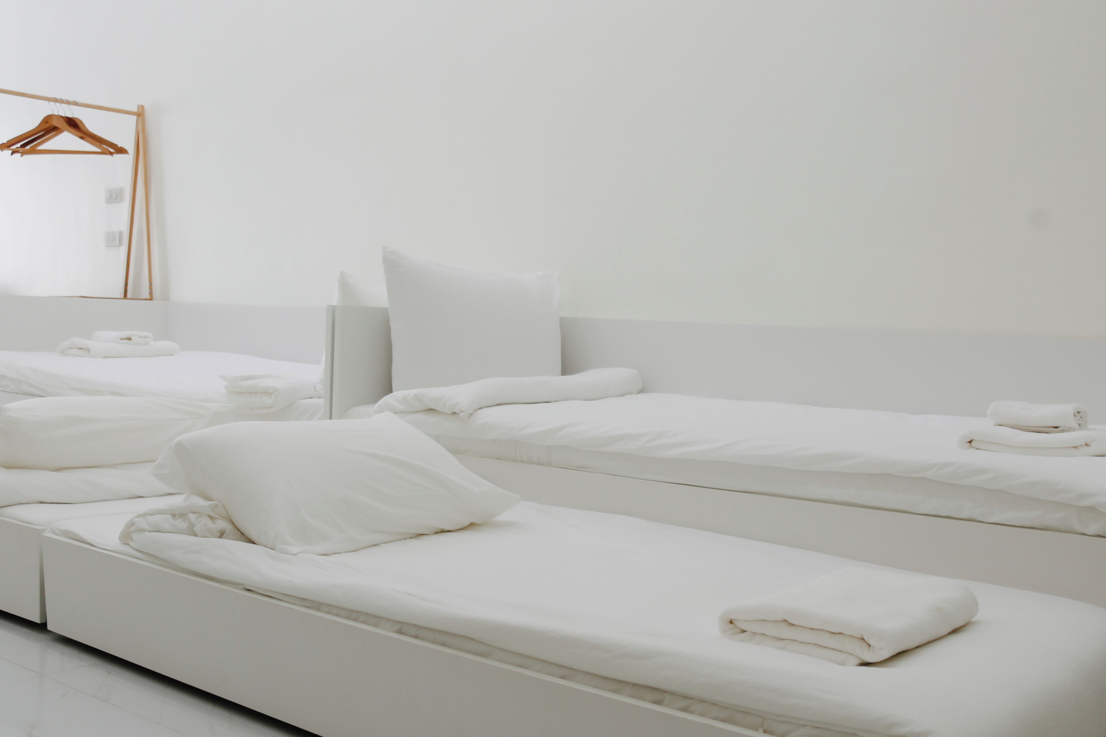 A hotel room with three single beds, a wooden hanger, and a mirror on the wall.