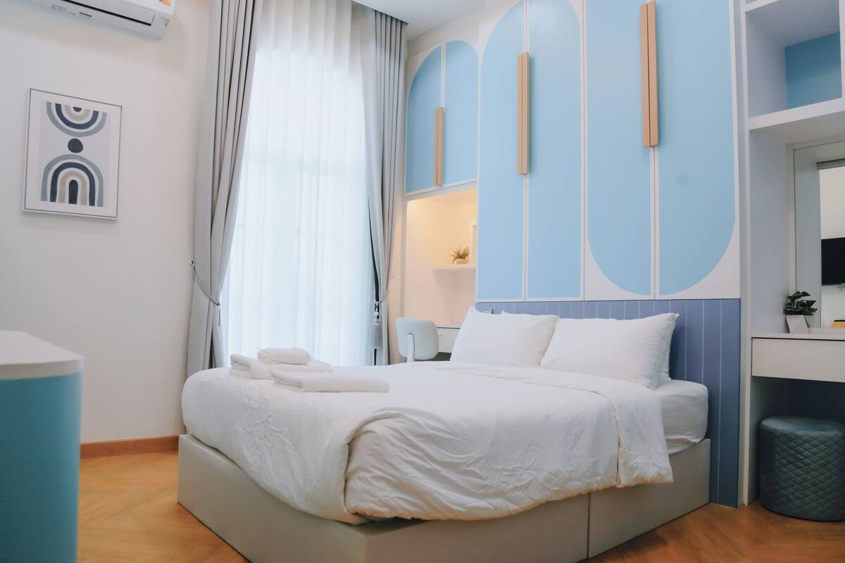 A modern hotel room with a large bed, a desk, and a window with curtains.