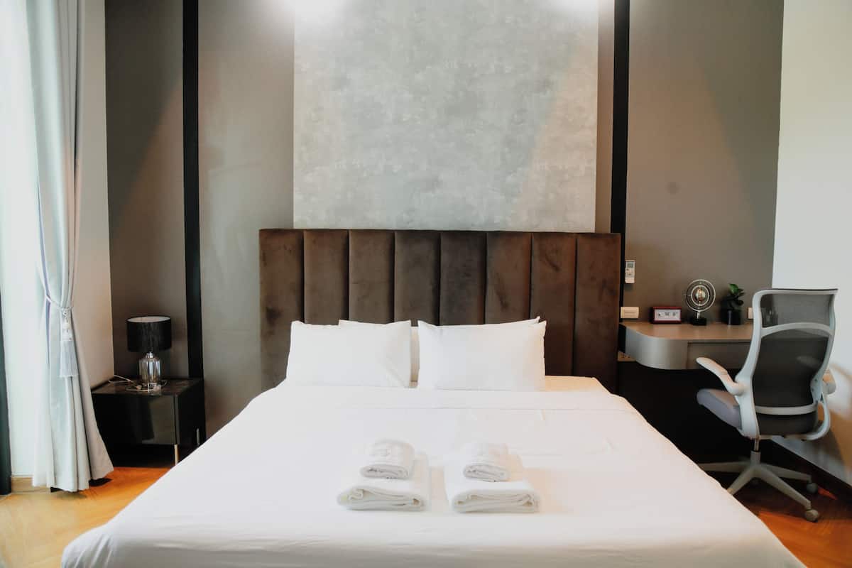 A hotel room with a bed, a desk, a chair, a lamp, and a wall-mounted artwork.
