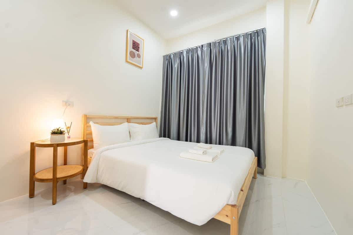 A neatly made bed with white linens, a wooden headboard, and a bedside table with a lamp and a small plant.