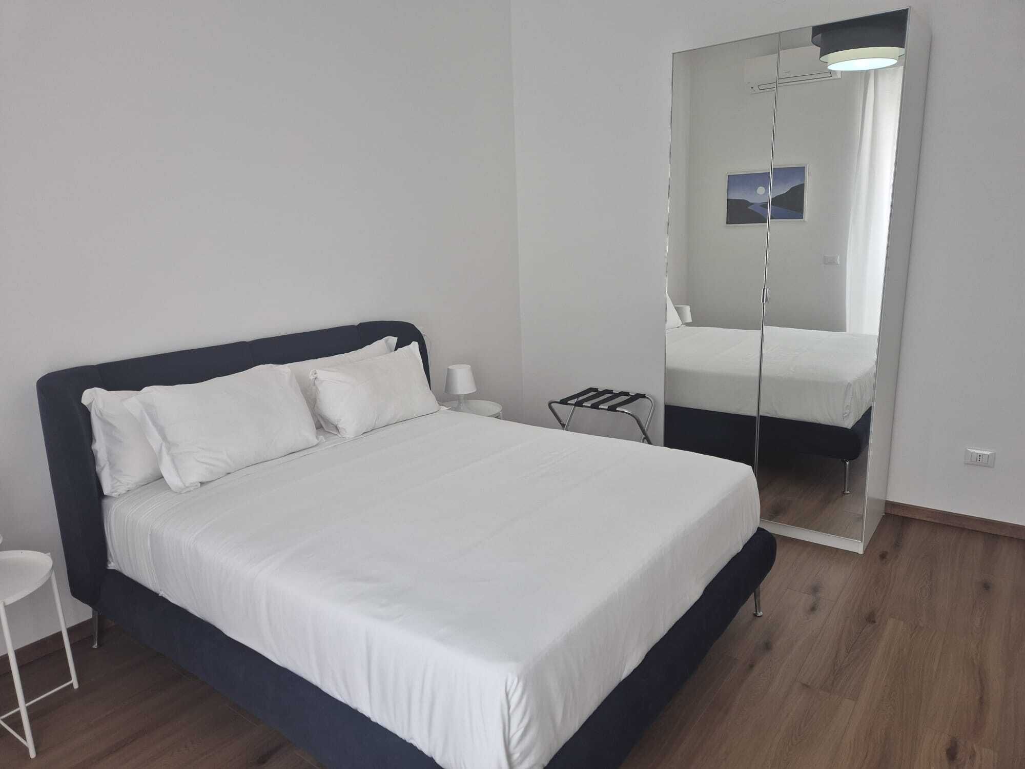 A modern bedroom with a large bed, a bedside table, a mirror, and a small stool.
