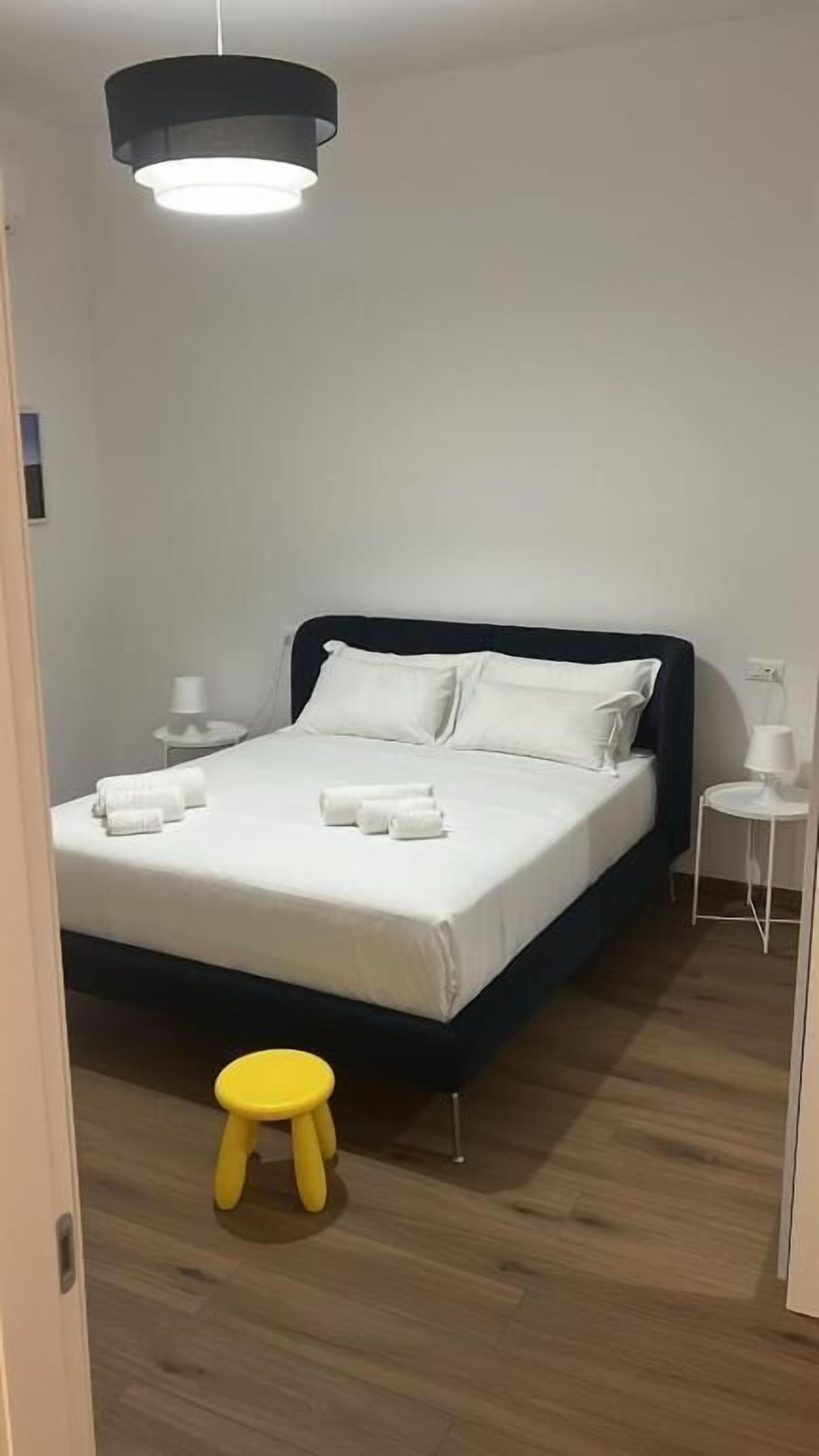A bedroom with a bed, bedside tables, a small stool, and a hanging light fixture.