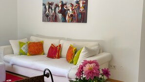 Un canapé blanc agrémenté de coussins colorés, un tableau au-dessus et un vase de fleurs posé sur une table.